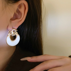 Primo piano di orecchini vintage rotondi in metallo dorato e resina bianca su modella