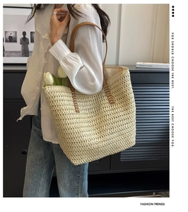 Detail of a large straw tote bag with brown handles and contrast stitching on woven texture