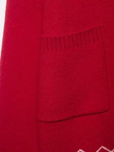 Dettaglio della giacca in maglia rossa con tasca strutturata e motivo jacquard bianco