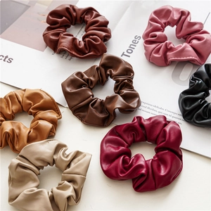 Set of seven colorful PU leather hair scrunchies flat laid on a magazine background