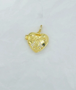 Detail of gold heart locket pendant with religious engraving and bow decorative top