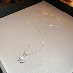 Macro detail of elegant gold necklace featuring a round white pearl and zircon pendant