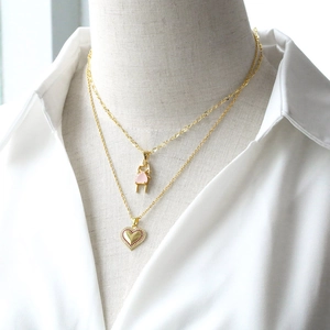 Layered gold necklaces with pink girl pendant and red zircon heart charm on white shirt