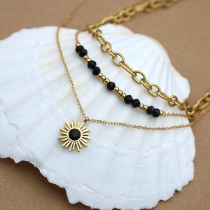 Detailed view of triple-layered golden necklace with black beads and sunburst pendant on shell