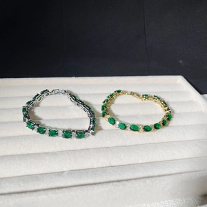 Detailed macro view of emerald green oval zircons on gold and silver chain bracelets