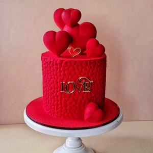 Détail du décor de gâteau cœur rouge avec texte LOVE doré sur un support blanc épuré