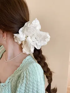 Detail of a large white lace scrunchie with floral embroidery worn on a bun hairstyle