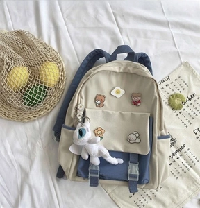 Detail view of cream and navy student backpack with cartoon patches and dragon plush charm