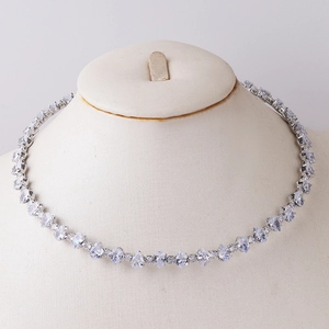 Detail of silver tennis necklace with heart and teardrop zircons on a beige mannequin