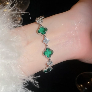 Nahaufnahme eines funkelnden grünen Kleeblatt-Armbands am Handgelenk mit flauschigem Ärmel