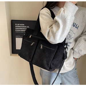 Detail of black corduroy tote bag featuring three front zip pockets and wide shoulder strap