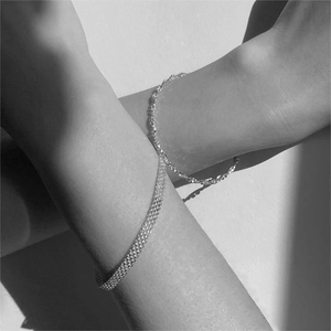 Artistic monochrome photo of woven mesh and twisted rope silver bracelets on crossed arms