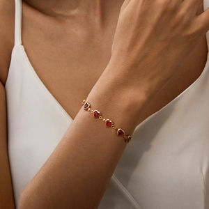 Close-up of a gold link bracelet featuring vibrant red heart-shaped charms on a wrist