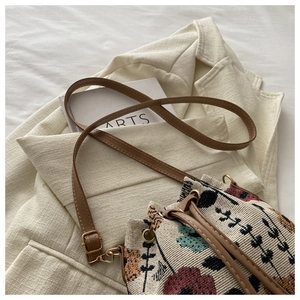 Detail of woven floral bucket bag with brown leather strap on a beige blazer background