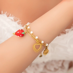 Detail of gold layered bracelet with red strawberry charm and hollow heart pendant