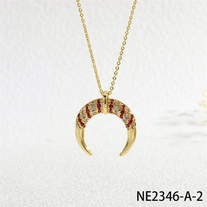 Close-up of gold horn pendant necklace with inlaid red and white zircons on white surface