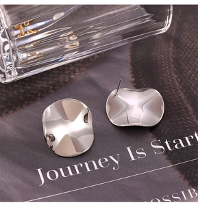 Macro shot of silver irregular wave disc studs with pleated texture and metallic finish