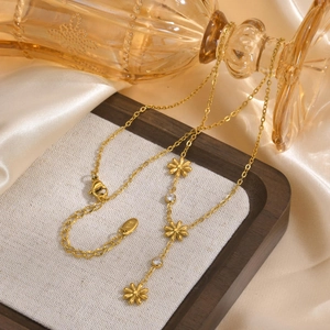 Golden stainless steel Y-shaped necklace with flower charms and clear zircon on a wooden tray