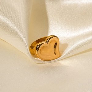 Detail of a chunky 18K gold-plated heart ring on elegant beige silk fabric