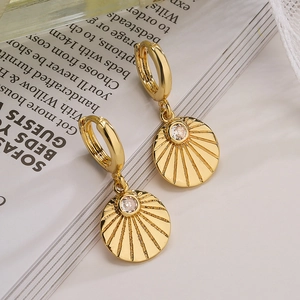Goldene Ohrringe mit Sonnenstrahl-Anhänger und Zirkon auf Lifestyle-Hintergrund