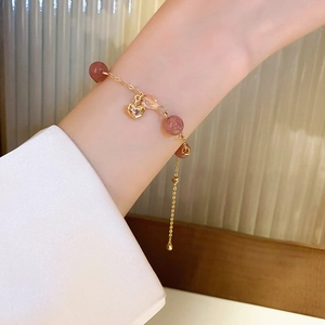 Close-up of heart-shaped strawberry crystal pendant on gold-tone chain bracelet