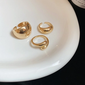 Macro detail of three minimalist golden organic droplet rings on a white ceramic plate
