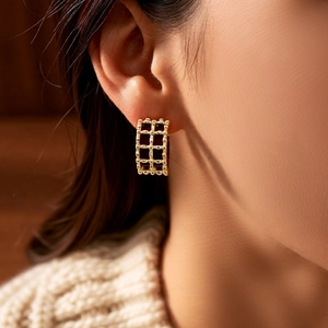 Close-up of 18K gold plated hollow grid earrings worn by a model in warm lighting