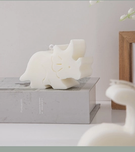 Detailed view of a triceratops dinosaur candle in cream white on aesthetic book props
