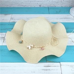 Détail d'un chapeau en paille crème avec bord ondulé et décorations florales