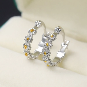 Close-up of silver and gold daisy hoop earrings on a soft beige velvet jewelry box