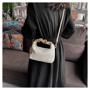 Detail of white pleated cloud bag featuring brown ruffled handle and metallic pendant