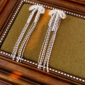 Detailed view of silver bow-knot tassel earrings with zircon inlay on green fabric