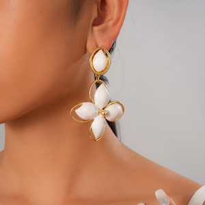 Close-up of gold oval hollow earrings with white enamel flowers worn by a model