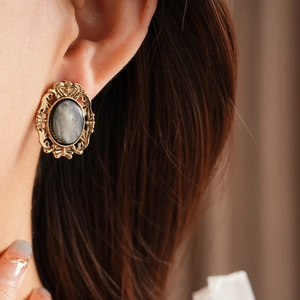 Close-up of vintage resin earring with engraved gold frame and dark gray oval stone