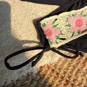 Detail of handcrafted crochet flower on high-waisted black bikini with pink floral accents