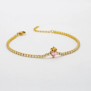 Detail of golden tennis bracelet featuring a pink heart zircon and a mini crown charm
