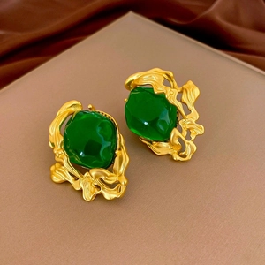 Détail de boucles d'oreilles dorées vintage avec résine vert émeraude irrégulière