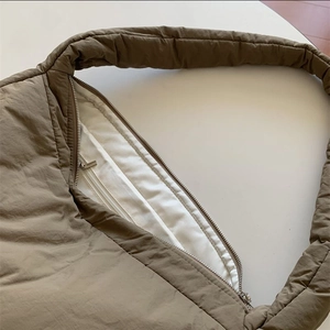 Detail view of brown quilted tote bag showing smooth zipper and white fabric lining