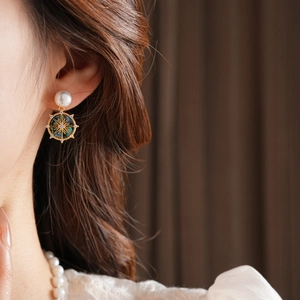 Close-up of model wearing gold starburst pearl earrings with abalone shell insets