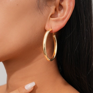 Close-up of a large polished gold hoop earring worn by a model for a modern look