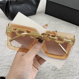 Detalle de gafas de sol cuadradas ámbar con una llamativa cadena decorativa de metal dorado