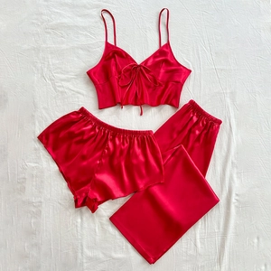 Three-piece red satin pajama set with camisole, shorts, and trousers on white bedding