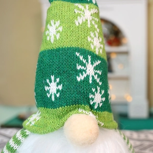 Close-up of green knitted Christmas gnome hat with white snowflake pattern and plush beard