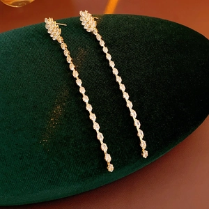 Detail shot of gold tassel earrings with zircon stones on green velvet jewelry pad