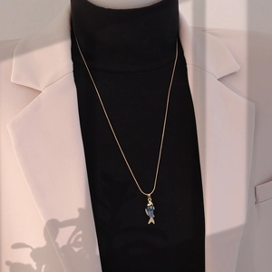Détail d'un collier pendentif carpe koi vintage porté sur un blazer beige chic