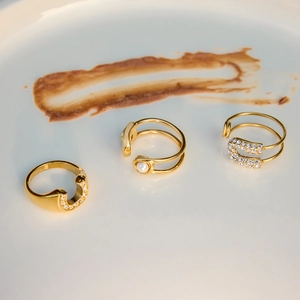 Detailed view of three 18K gold paperclip rings with pearls and zircons on a white plate