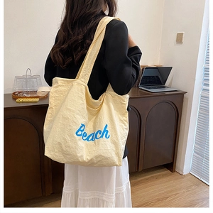 Close-up of yellow canvas tote bag with blue Beach print worn over a black blazer