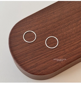Macro shot of minimalist S999 pure silver hoop earrings on a dark wood display