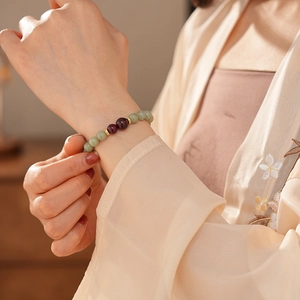 Detail of green jade and red agate beads bracelet on wrist with silk embroidery garment