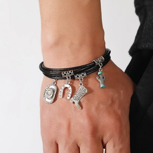 Detail of leather bracelet featuring cowboy hat and horseshoe charms with lucky engraving
